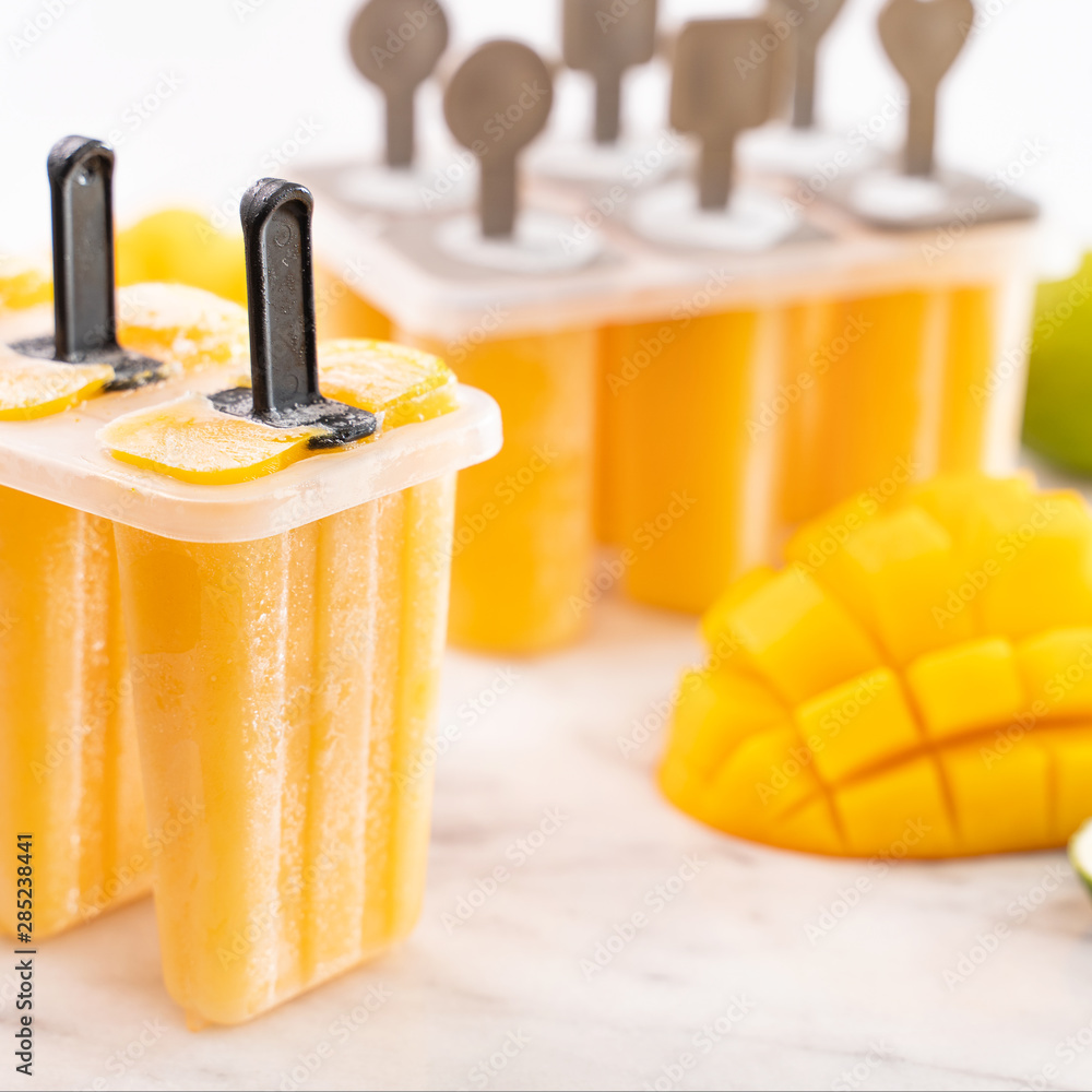 新鲜芒果果冰棍冰放在明亮大理石桌子上的塑料成型盒中。夏日心情概念