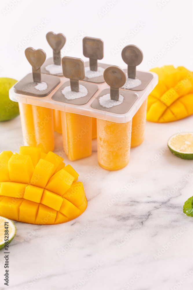 新鲜芒果果冰棍冰放在明亮的大理石桌子上的塑料成型盒中。夏日心情概念