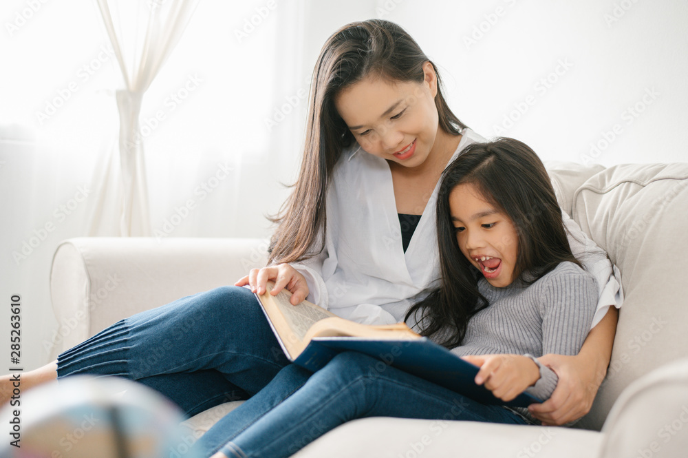 快乐的孩子，亚洲小女孩，在家里客厅的桌子上看书。家庭活动