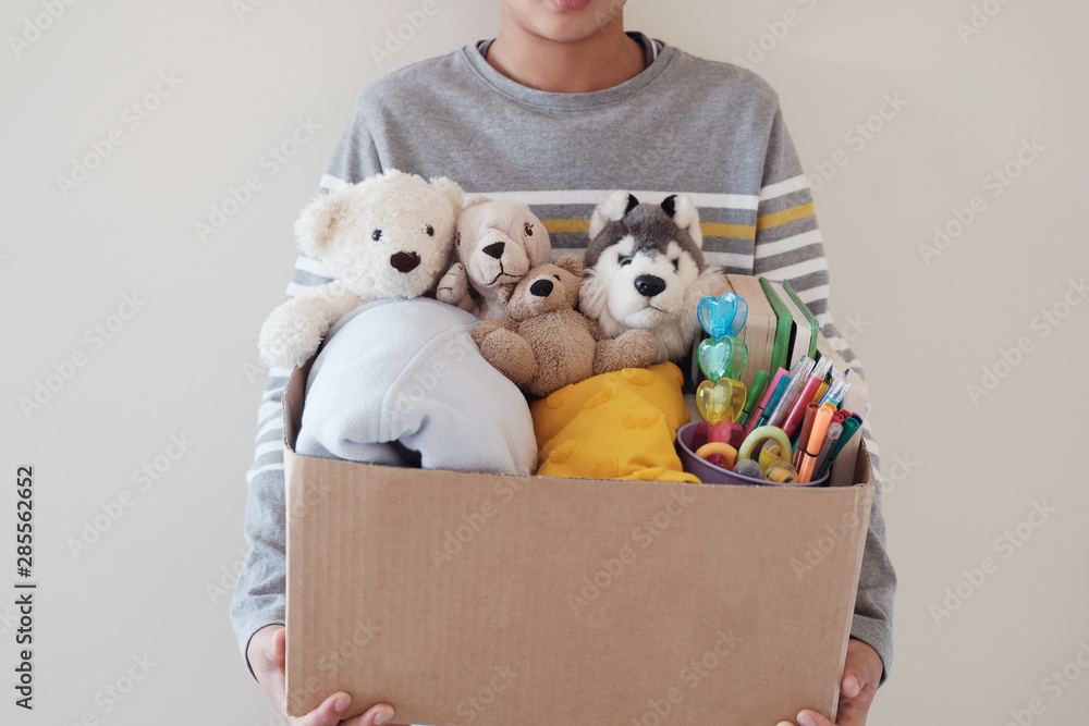 Young volunteer preteen teenage boy holding a box full of used toys, cloths, books and stationery fo