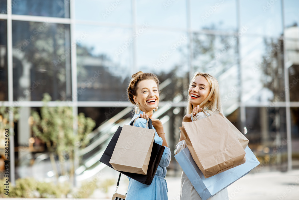 两个快乐的女人拿着购物袋站在商场前的画像