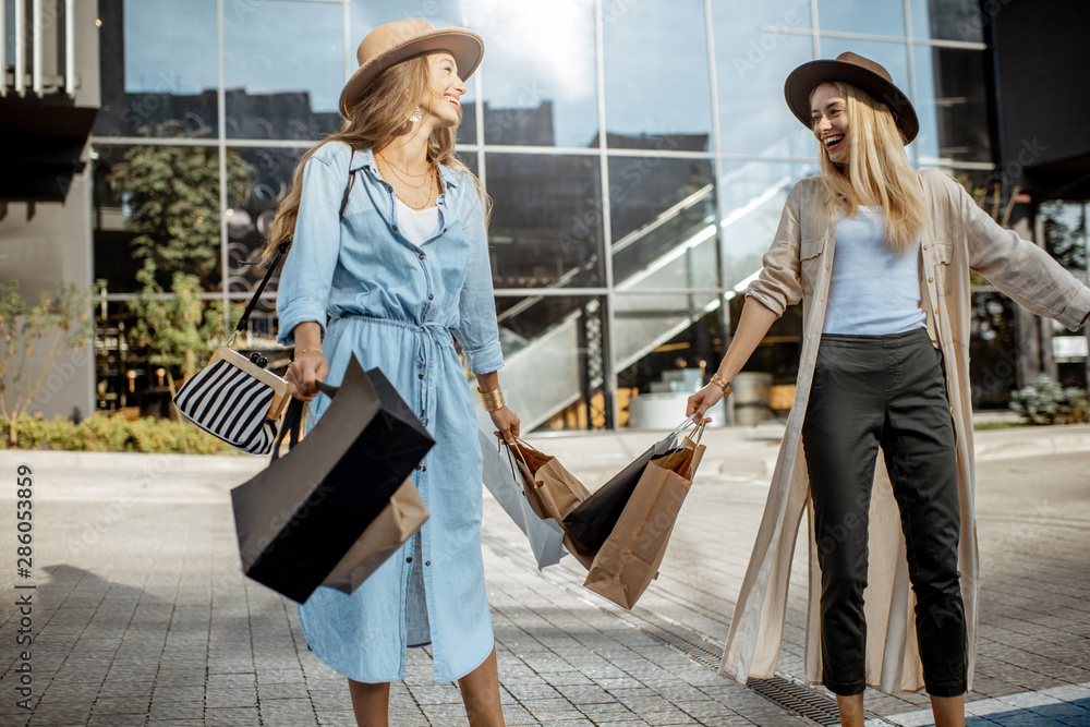 两个快乐快乐的女人拿着购物袋在商场前的画像，感觉很特别