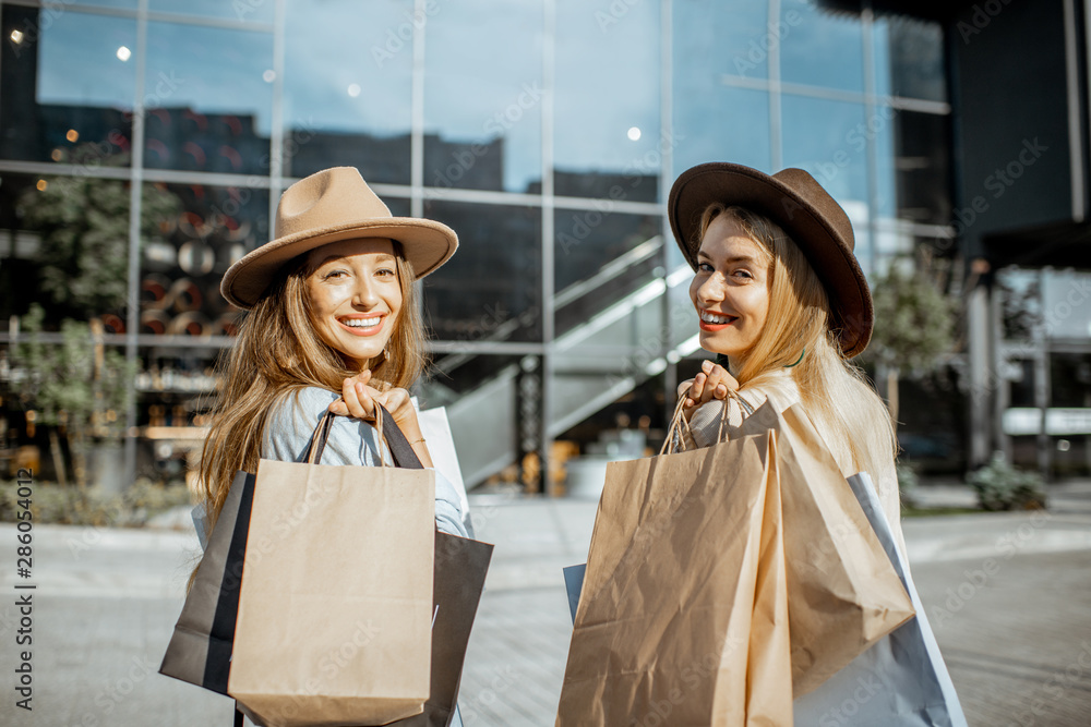 两个快乐的女人拿着购物袋站在购物中心前的画像