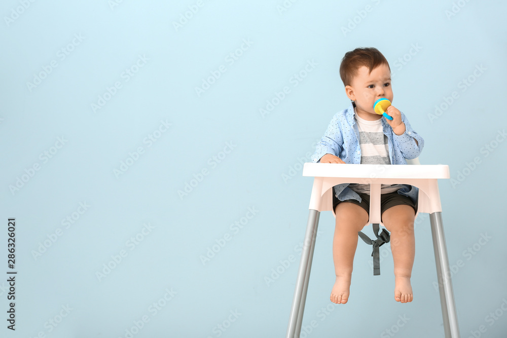 可爱的小男孩坐在彩色背景的高脚椅上