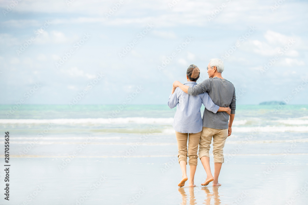 幸福的亚洲老年夫妇在海滩上玩得很开心，老年男女边走边拥抱