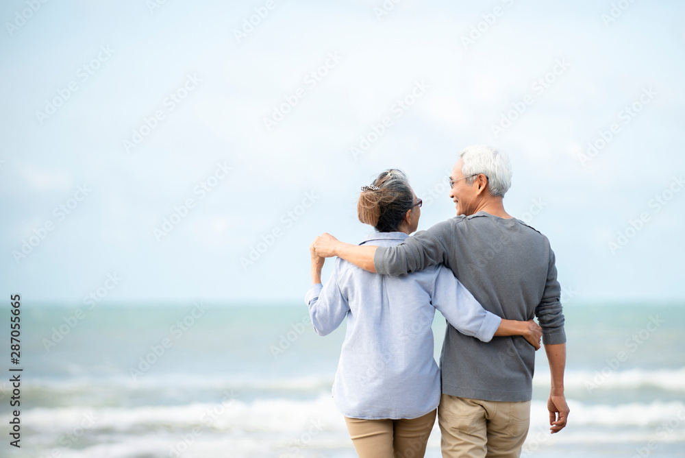 快乐的亚洲老年夫妇在海滩上玩得很开心，老年男女在散步时拥抱
