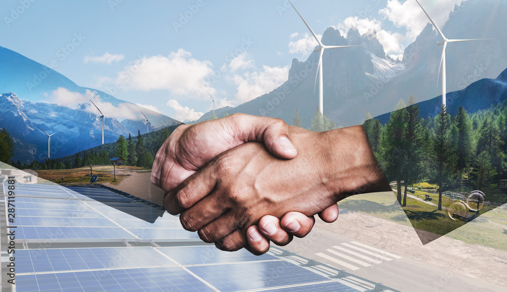 Double exposure graphic of business people handshake over wind turbine farm and green renewable ener