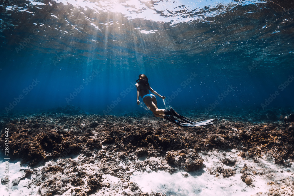 一名带鳍的自由潜水女子在蓝色海洋中的珊瑚上滑翔。