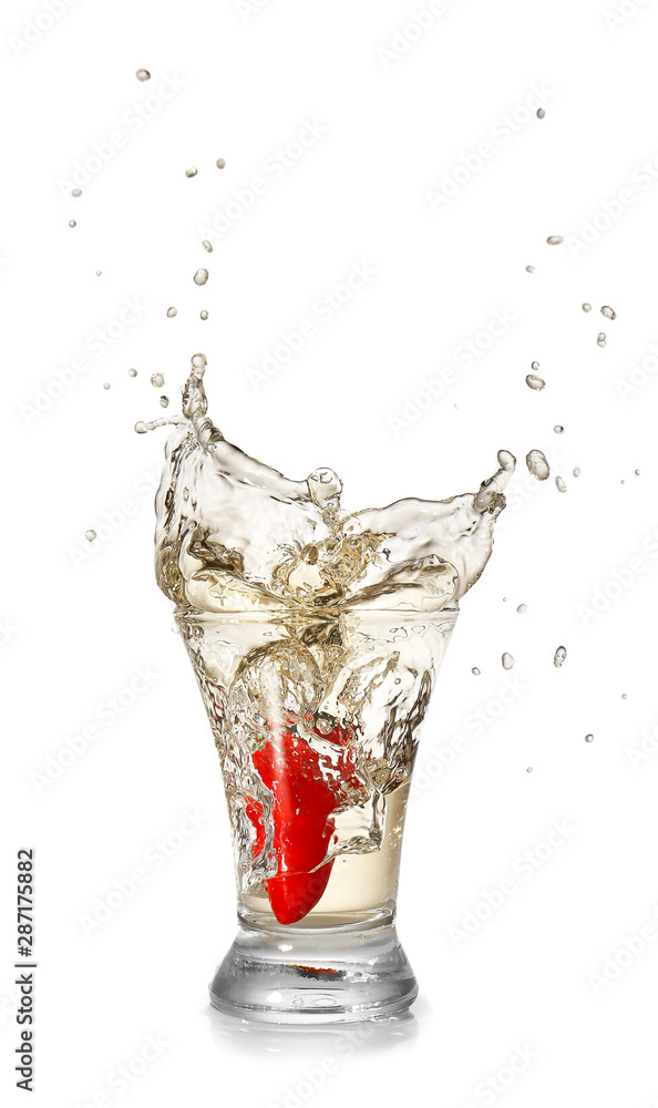 Dropping of chili pepper into glass with tasty tequila on light background