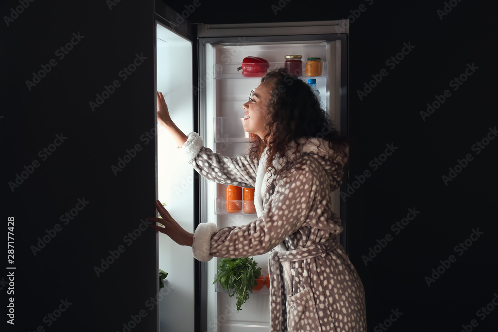 年轻女子晚上在冰箱里挑选食物
