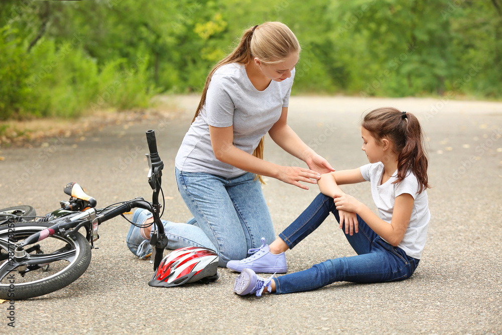 母亲在户外帮助从自行车上摔下来的小女儿