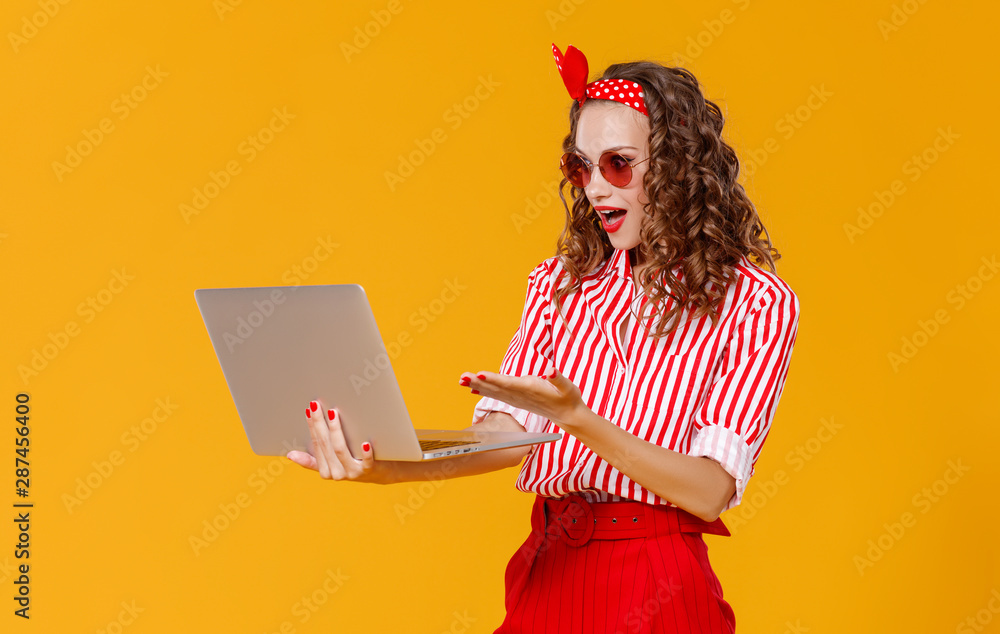 黄色背景下拿着笔记本电脑的风趣开朗的女人。