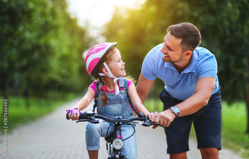 幸福家庭的父亲教孩子女儿在公园里骑自行车。