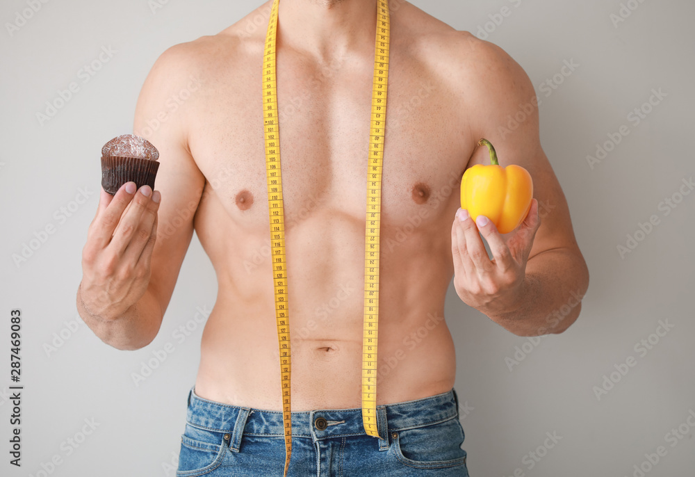 Handsome muscular man with measuring tape, healthy and unhealthy food on light background. Weight lo