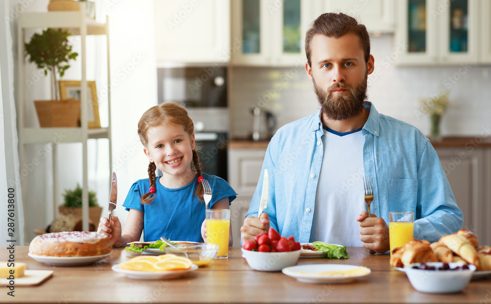 幸福的家庭父亲带着孩子在厨房里用早餐喂养他的女儿。