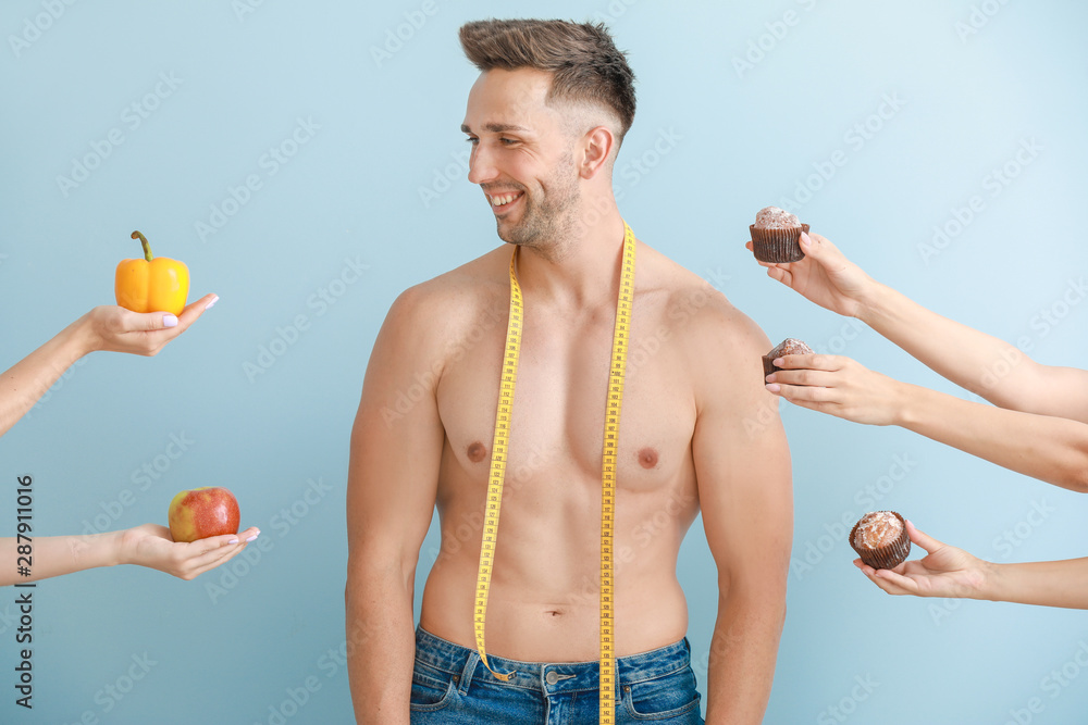 Handsome muscular man with measuring tape and hands suggesting him different food against color back