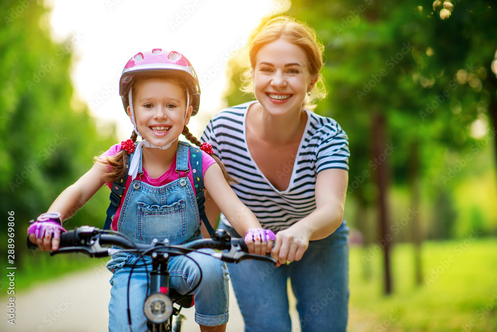 幸福的家庭母亲教孩子女儿在公园里骑自行车