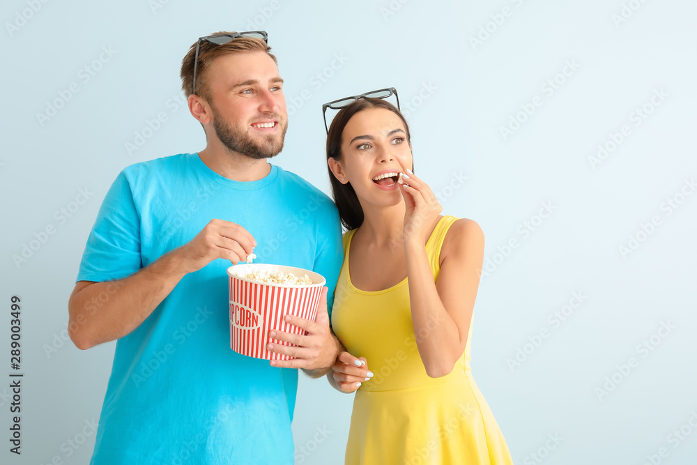 Young couple with popcorn watching movie on light background