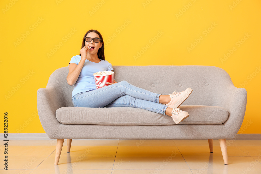拿着爆米花的年轻女子在靠近彩色墙的沙发上看电影