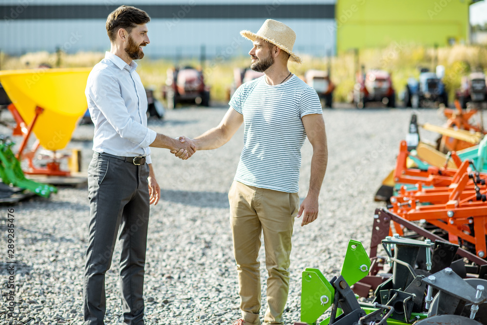 Agronomist shaking hand with salesman, having a deal about purchase a new agricultural machinery on 