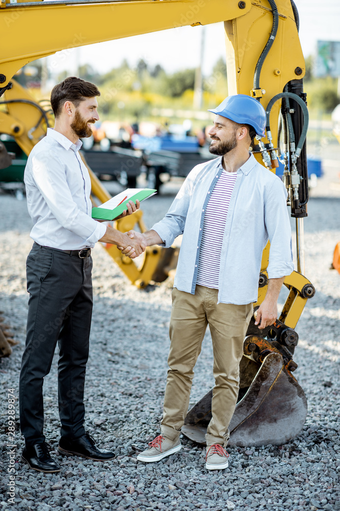 Builder choosing heavy machinery for construction shaking hands with a sales consultant on the open 