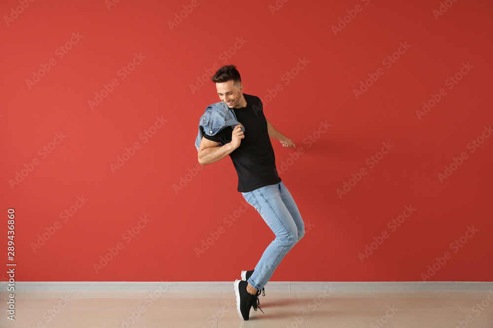 Handsome young man dancing against color wall