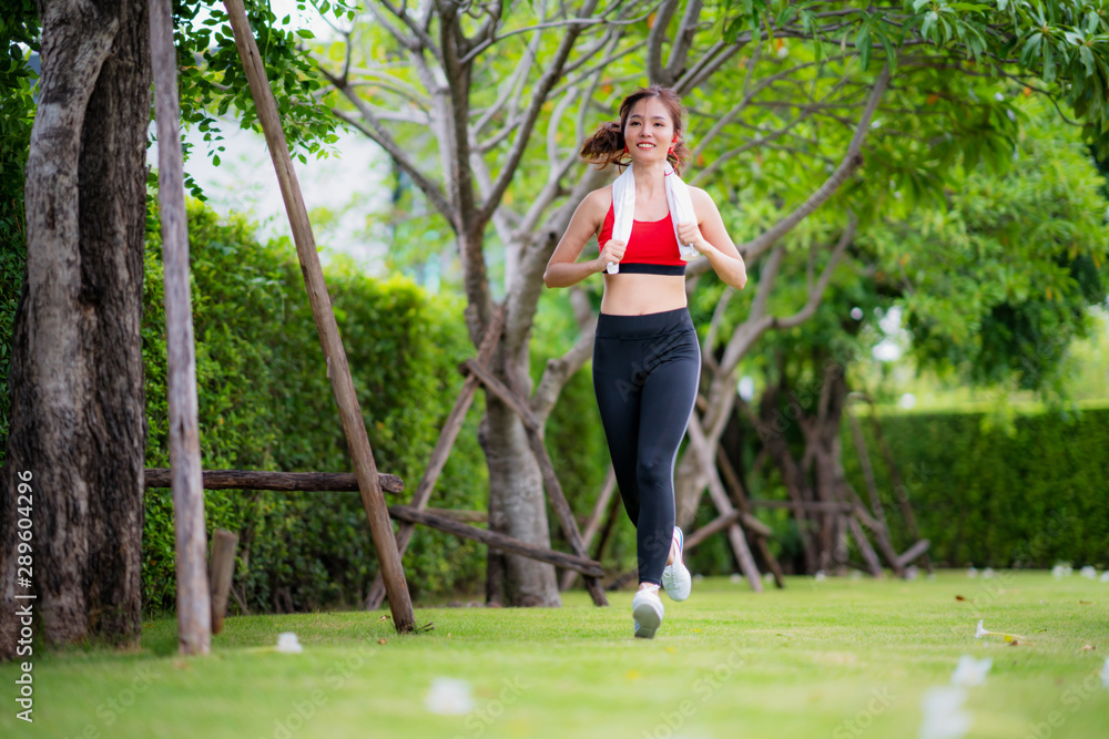 在美丽的夏日，慢跑的女人在阳光下的公园里跑步。运动健身模特亚洲人
