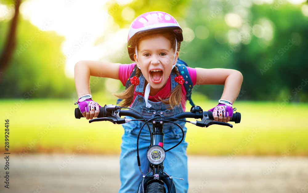 快乐快乐的小女孩在大自然的公园里骑自行车。