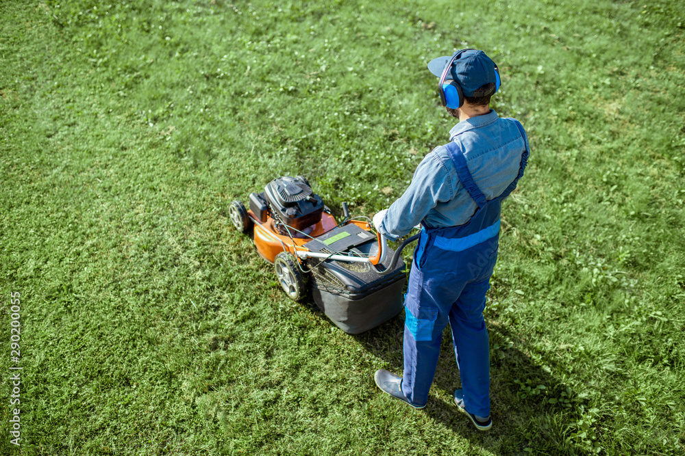 穿着防护服的专业园丁在后院用汽油割草机割草，