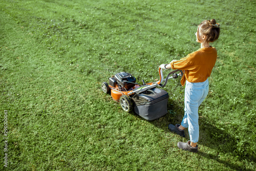 漂亮的年轻女人用汽油割草机割草，在后院园艺