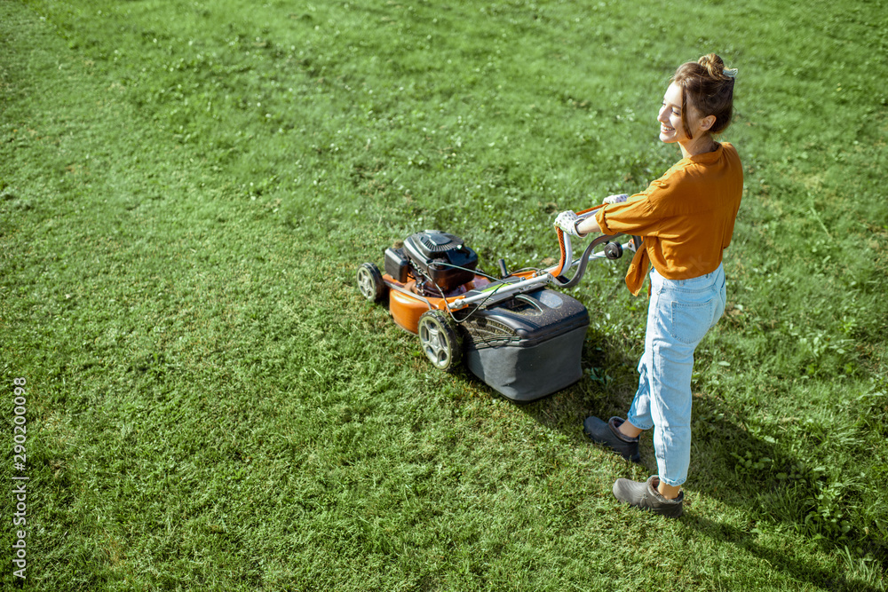 漂亮的年轻女人用汽油割草机割草，在后院园艺