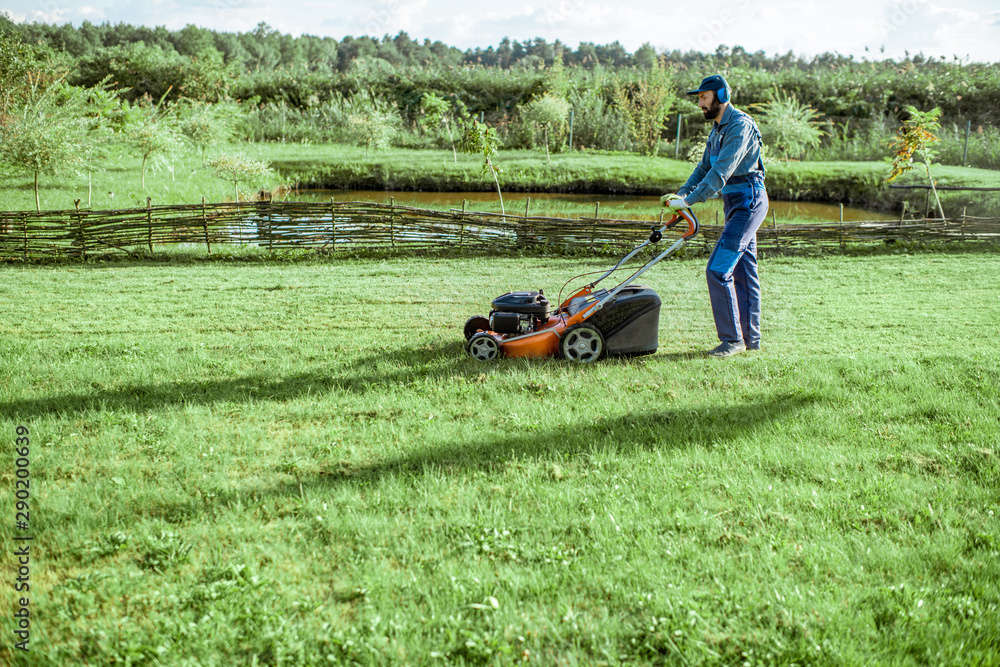 穿着防护服的专业园丁在美丽的土地上用汽油割草机割草