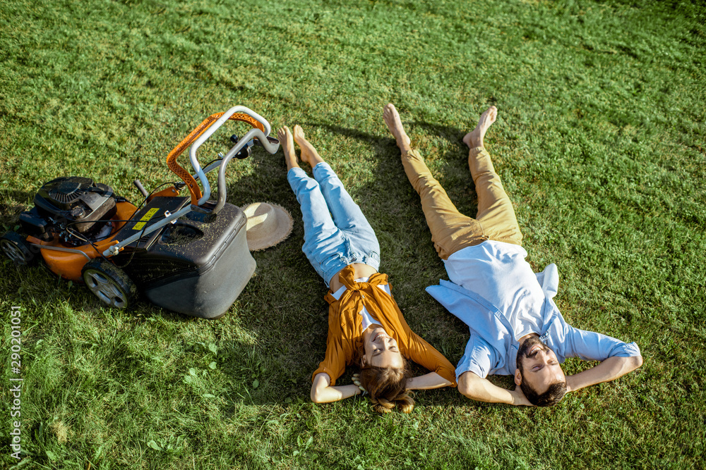 美丽的男人和女人在割草机附近的草地上休息，在后院享受园艺