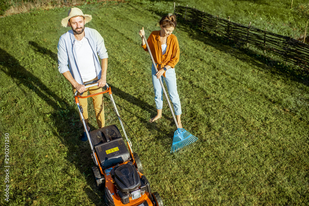 男女清洁绿色草坪，用割草机割草，用耙子扫树叶