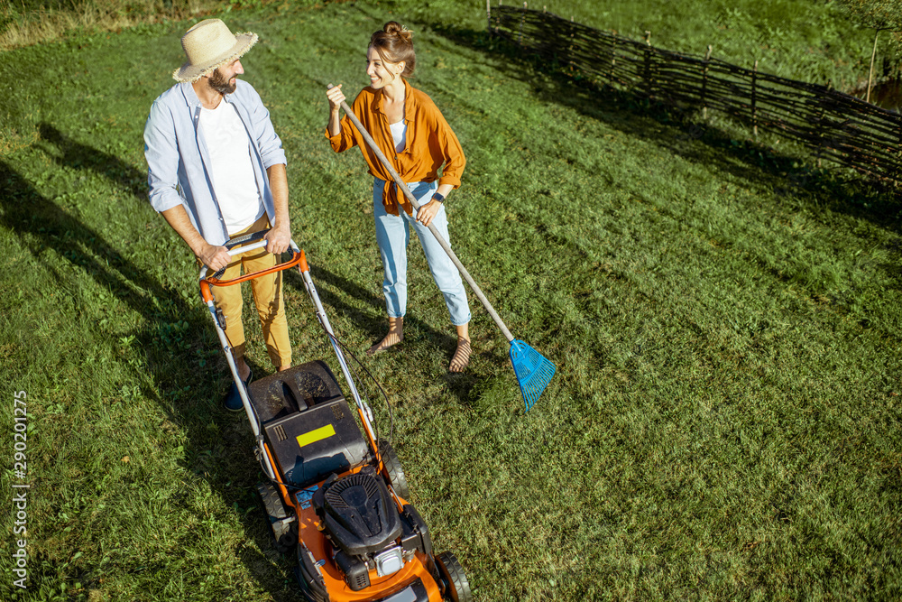 男男女女清洁绿色草坪，用割草机割草，用耙子扫树叶