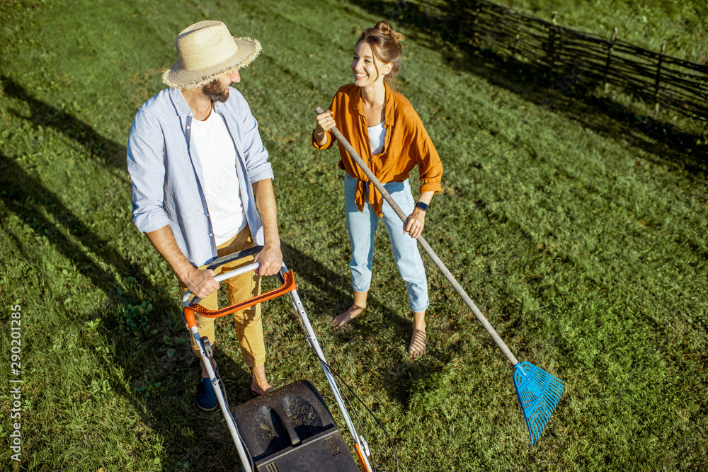 男女清洁绿色草坪，用割草机割草，用耙子扫树叶