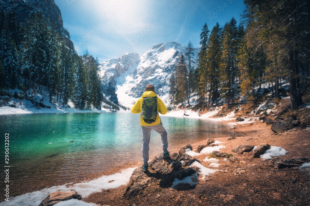 秋天阳光明媚，背着背包的运动男站在湖水湛蓝的湖边的石头上