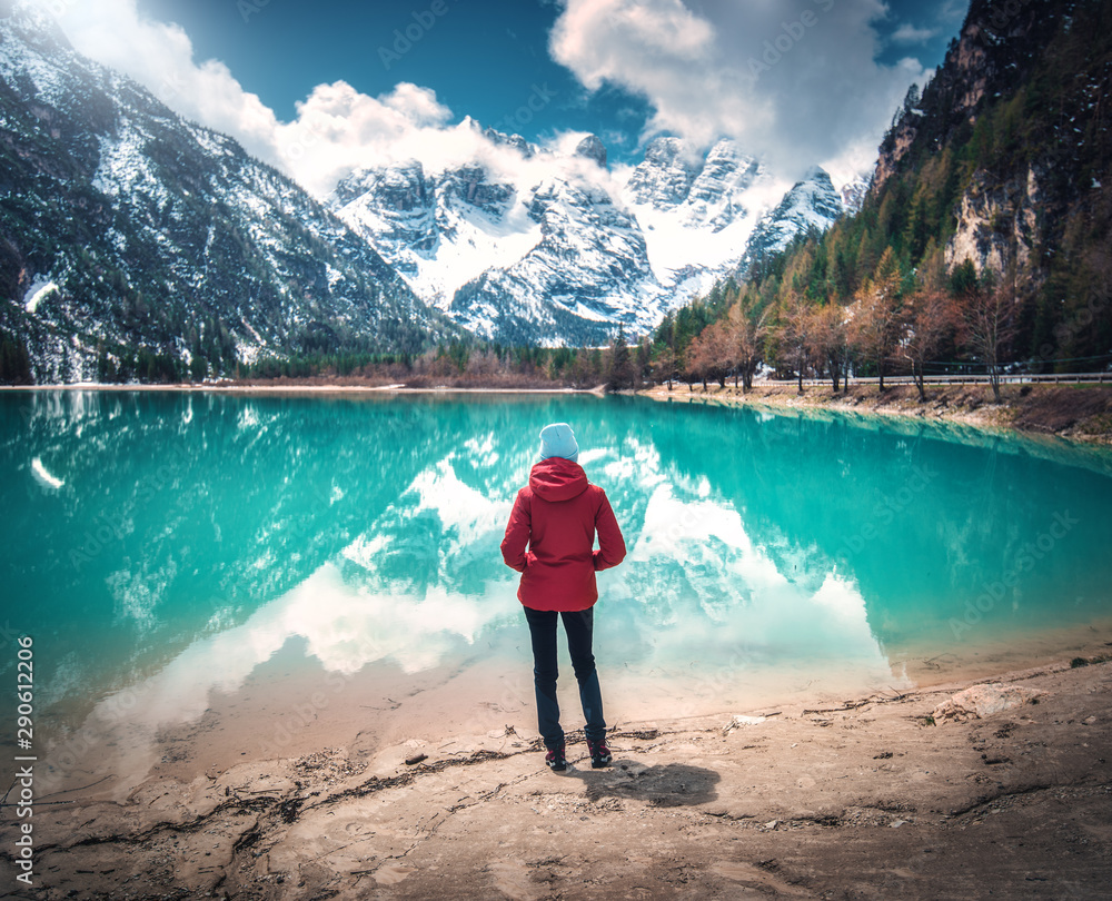 在秋天阳光明媚的日子里，穿着红色夹克的年轻女子站在湖水湛蓝的湖边。旅行。兰