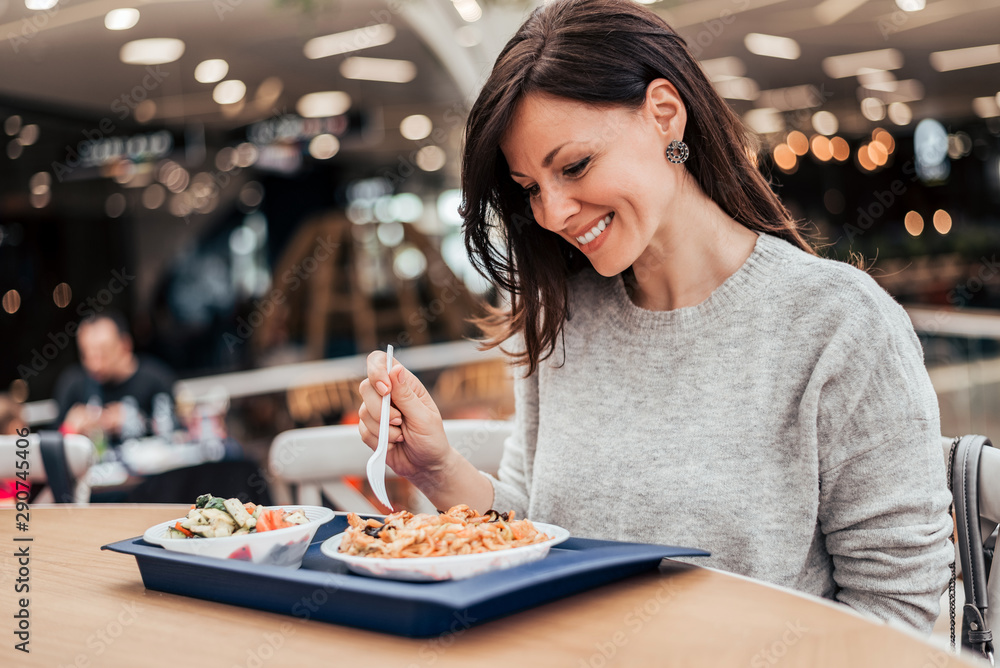 一个微笑的女人在美食广场吃午饭的肖像。