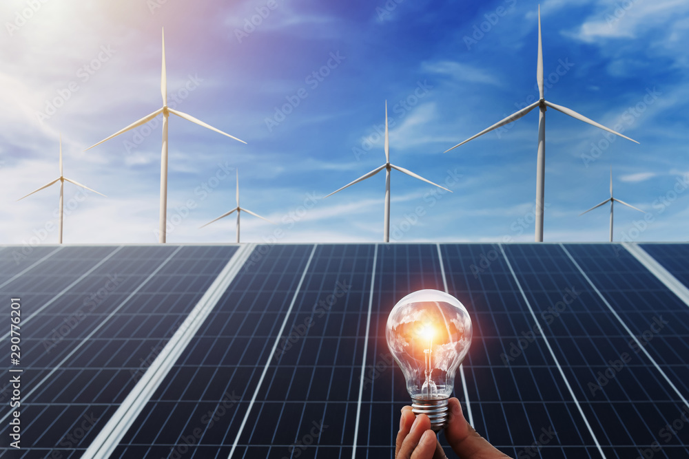 太阳能电池板和风力涡轮机背景的手持灯泡。自然中的清洁能源概念