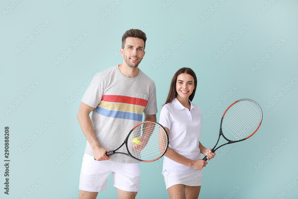 Young couple with tennis rackets on color background