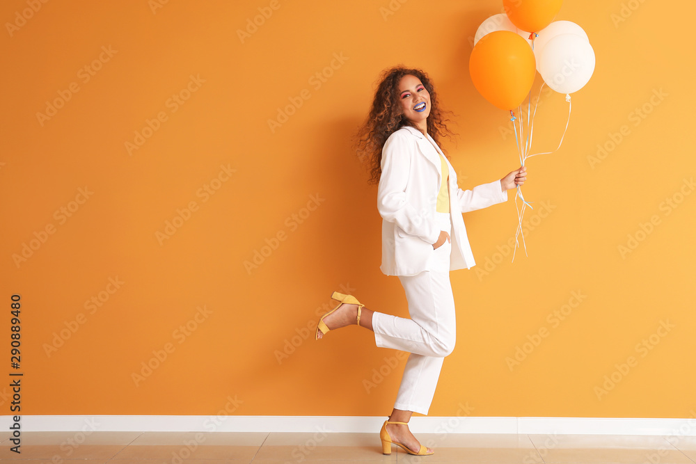 Fashionable young African-American woman with balloons against color wall