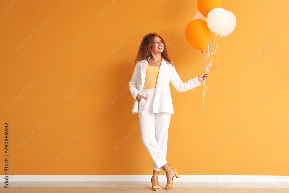 时尚的年轻非裔美国女性，靠着彩色墙拿着气球