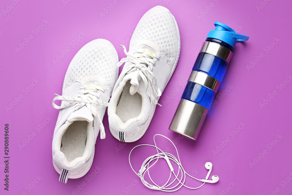 Sports water bottle, shoes and earphones on color background