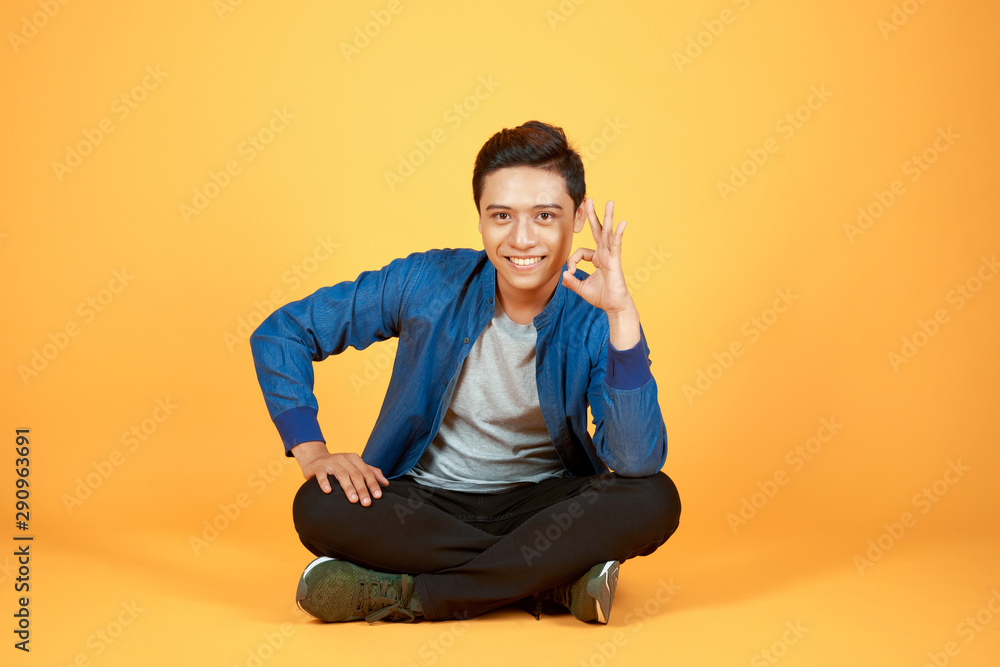 年轻休闲的亚洲男子盘腿坐着，抱着头，对着镜头微笑。i