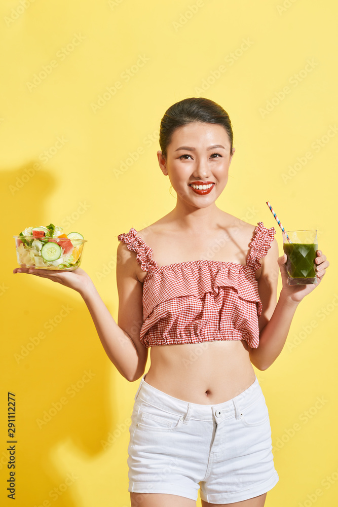 漂亮的亚洲女人拿着沙拉碗和绿色果汁