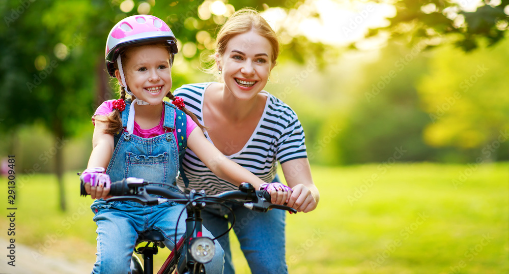 幸福的家庭母亲在公园里教孩子女儿骑自行车。