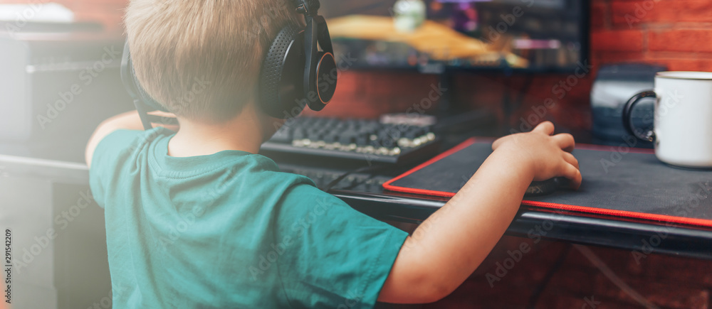 小男孩戴着带麦克风的耳机在电脑上玩游戏，电脑游戏