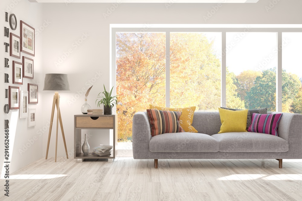 时尚的白色房间，窗户里有沙发和秋天的风景。斯堪的纳维亚室内设计。