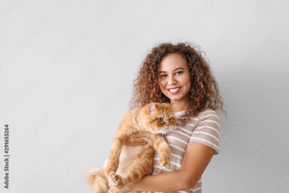 Young African-American woman with cute cat on light background